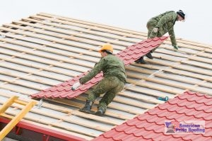 workers installing red metal panels on roof